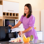 Mulher na cozinha preparando batatas e brócolis em uma air fryer compacta preta, ilustrando o modelo ideal para quem mora sozinho.