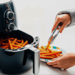 Pessoa servindo batatas fritas de uma air fryer preta usando um pegador de metal, exemplificando o uso correto ao evitar o que não pode ir na airfryer.