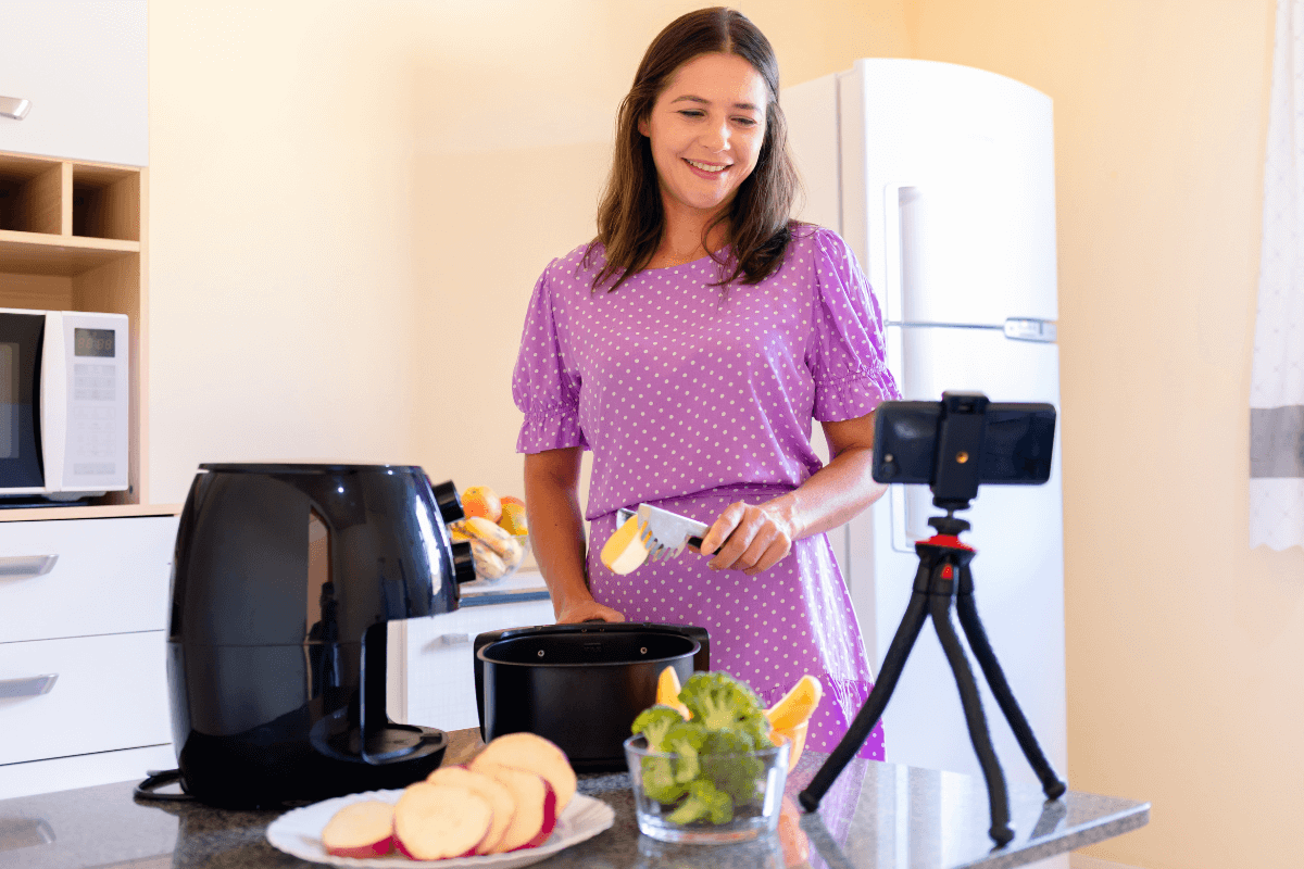Mulher gravando preparo de batatas e brócolis na airfryer, demonstrando na prática se o eletrodoméstico vale a pena no dia a dia.